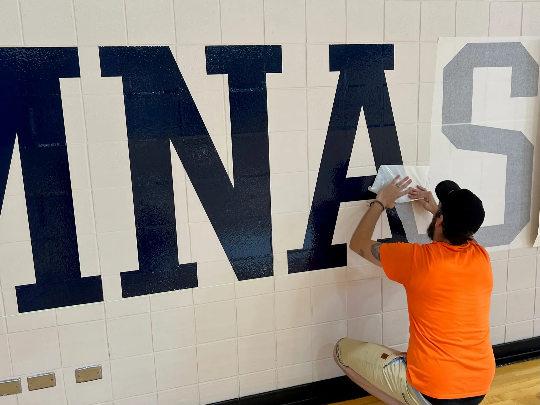 a person in an orange shirt painting a wall with blue letters