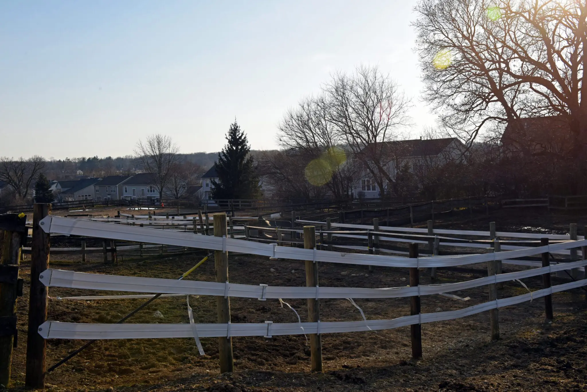a fenced in field with trees and houses in the background
